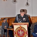 Druh ubrany w mundur galowy wstaje i przemawia przez mikrofon z mównicy.