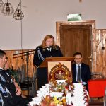 Kobieta ubrana w mundur galowy odczytuje sprawozdanie przez mikrofon na mównicy.