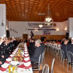 Druhowie i druhny podnoszą kartki do głosowania. Siedzą przy zastawionych stołach z czerwonymi obrusami