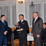 Mężczyźni ubrani w czarny garnitur i mundur galowy składają podziękowania mężczyźnie ubranego w granatowy garnitur.