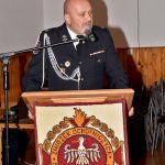 Mężczyzna ubrany w strażacki mundur galowy przemawia z mównicy.