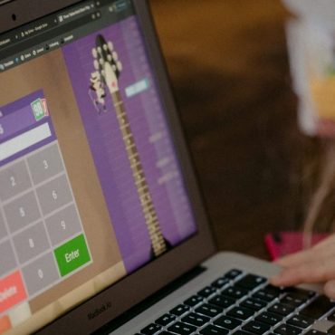 Młoda dziewczyna z kręconymi brązowymi włosami siedzi przy laptopie ucząc się tabliczki mnożenia
