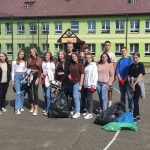 Kilkunasto-osobowa grupa nastoletnich chłopców i dziewcząt pozuje do fotografii na boisku przed szkołą. Przed nimi znajdują się wypełnione worki ze śmieciami.