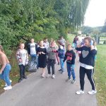 Grupa dzieci przechodzących drogą i zbierających śmieci. W tle drzewa.