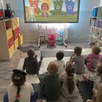 Grupa dzieci siedzących w klasie pilnie spoglądających na tablicę na której znajduje się grafikę o wymowie ekologicznej.