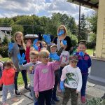 Kilkuosobowa grupa dzieci z dwoma Paniami nauczycielkami. Dzieci mają ubrane gumowe rękawiczki.