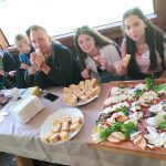 Grupa młodzieży wraz z dorosłym opiekunem, zasiadający przed obficie zastawionym, dużym stole.