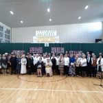 Grua kilkudziesięciu osób pozuje do wspólnego zdjęcia w jasnej sali gimnastycznej.