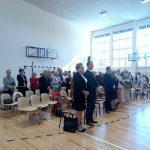 Grupa osób stoi w jasnej sali z duzymi oknami.