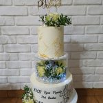 Duży trzy warstwowy tort jasny kremowy przyozdobiony świezymi kwiatami.