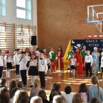 Grupa odświętnie ubranych dzieci występujących w sali gimnastycznej.