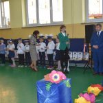 Kobieta ubrana w zieloną marynarkę przemawia do mikrofonu na sali.