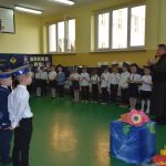 Ksiądz ubrany na czaro przemawia do dzieci na sali gimnastycznej.