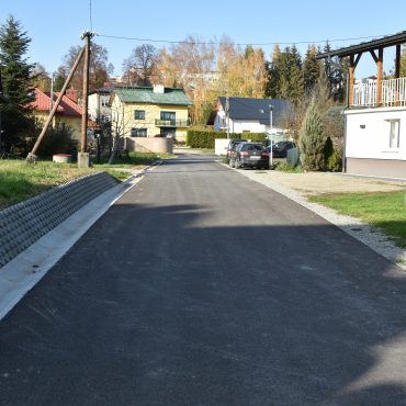 Droga z nową nawierzchnią asfaltową, miedzy budynkami.