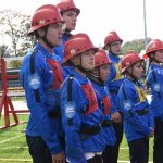 Grupa dzieci w strojach strażackich, pozujących w grupie do zdjęcia.