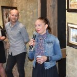 Kobieta i mężczyzna w średnim wieku stojący obok siebie. Kobieta przemawia za pomocą mikrofonu.