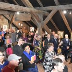 Grupa osób różnej płci i wieku na masywnym poddaszu. Zebrani rozmawiają i oglądają obrazy.