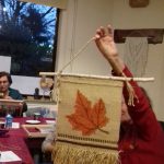 Kobieta w czerwonej bluzce pokazuje w ręce nowo wytkany obraz.