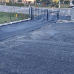 Asfaltowy plac. W tle widać krzewy i budynki.