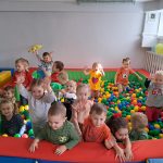 Grupa dzieci, chłopcy i dziewczynki bawią się w w basenie z kulkami. W rękach trzymają kolorowe maskotki.