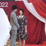 Młoda para, dziewczyna z ciemnej sukience i berecie oraz chłopak w marynarce w kratę spiewają na sali gimnastycznej.