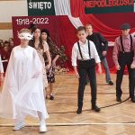 Grupa dzieci przebranych w różne stroje tańczy na sali gimnastycznej.