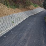 Droga z nowo położonym asfaltem. W tle skarpę podpartą płytami.