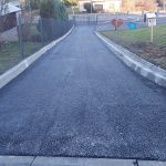 Asfaltowa droga. W tle ulica, budynki i krzewy.