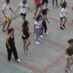 Grupa dzieci ubrana w krótkie stroje tańczy na kostce brukowej.