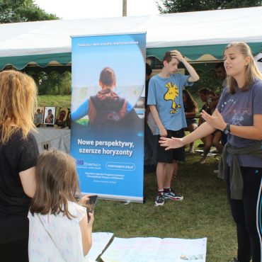 Grupa dziewczyn opowiada na zewnątrz przy plakacie.