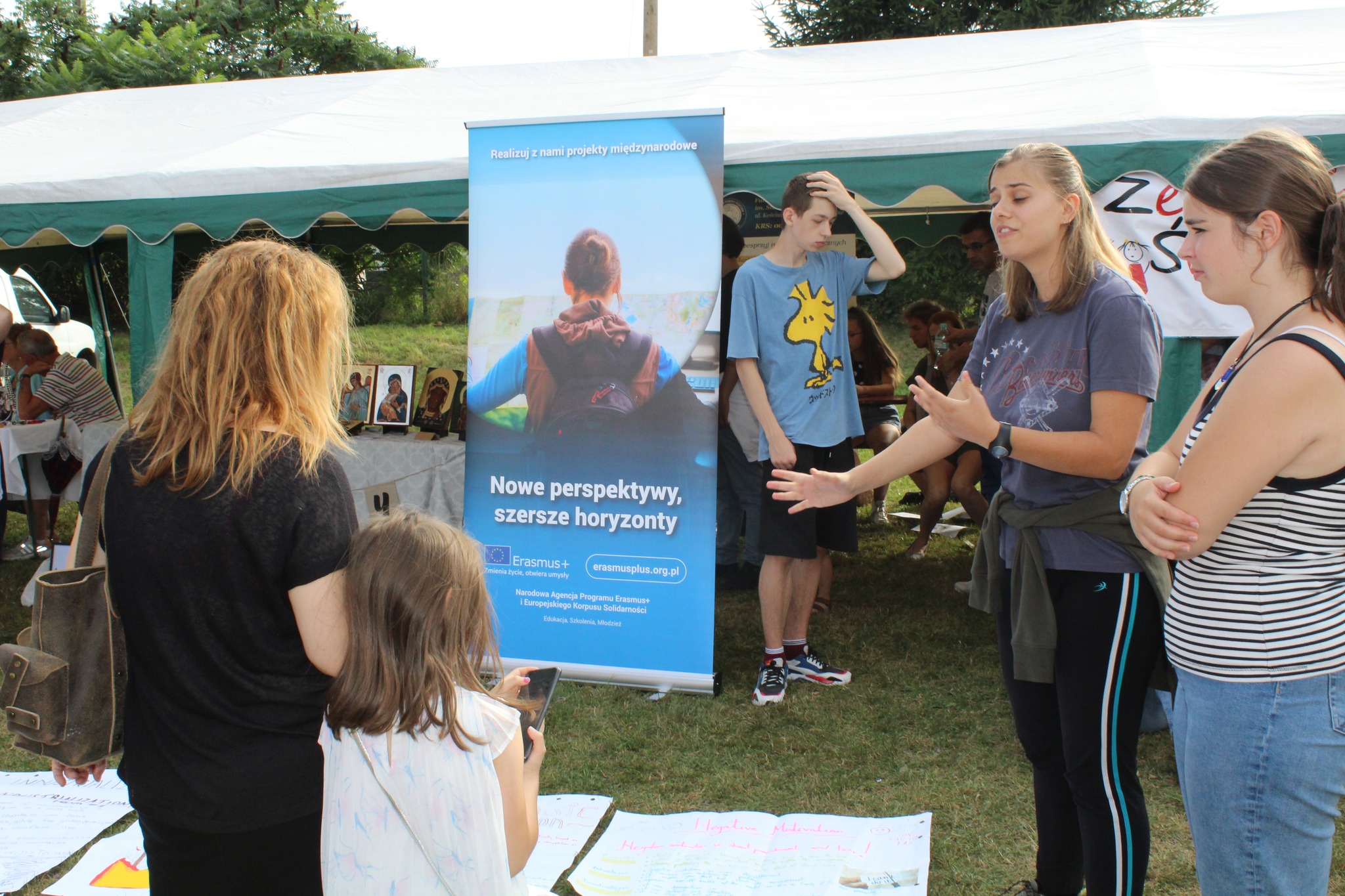 Grupa dziewczyn opowiada na zewnątrz przy plakacie.