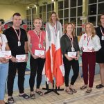 Grupa dorosłych kobiet i mężczyzn pozuje do zdjęcia przed basenem otwartym.