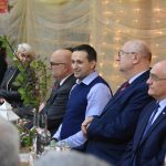 Mężczyźni siedzą przy stole, za nimi dekoracja ze światełek.