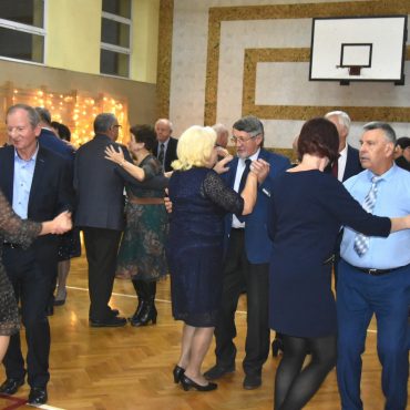 Grupa straszych osób tańczy na sali gimnastycznej.