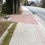 Chodnik z kostek brukowych oraz droga asfaltowa. W tle lampy, dom i krzewy.