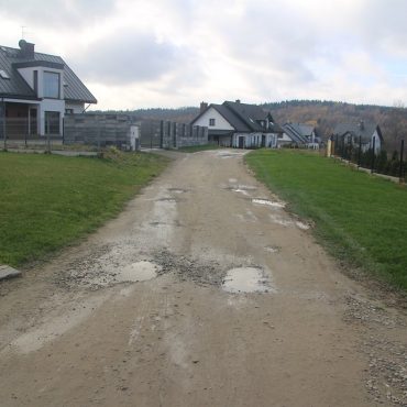 Droga z dziurami błonista pomiędzy nową zabudową mieszkalną.