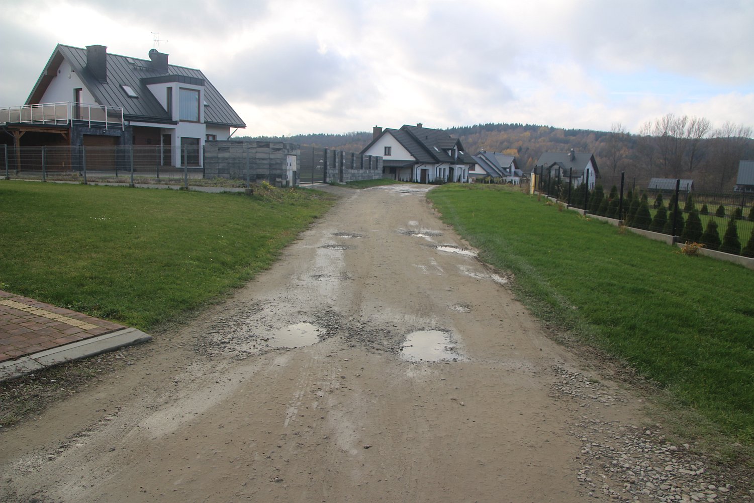 Droga z dziurami błonista pomiędzy nową zabudową mieszkalną.