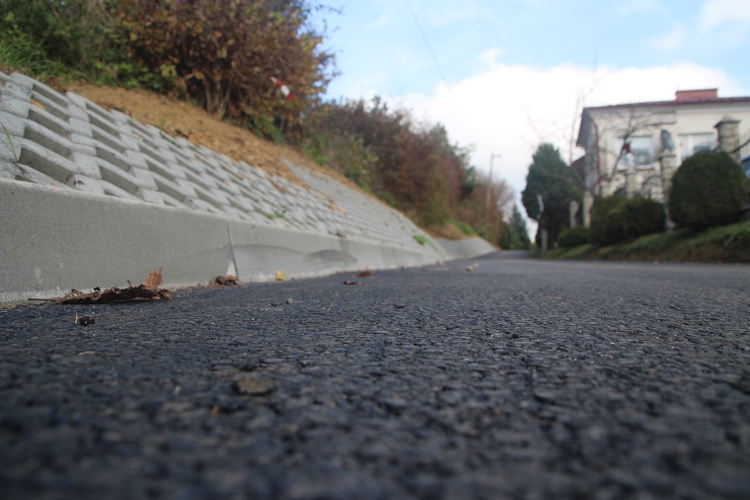 Droga z nowo położonym asfaltem. W tle widać budynek mieszkalny .