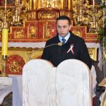 Dorosły mężczyzna ubrany w kurtkę i garnitur przemawia na ambonie w kościele.