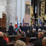 Kilka pocztów sztandarowych stojąca w kościele. W tle widać osoby siedzące na ławce.