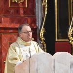 Meżczyzna ubrany w złoty ornat przemawia na ambonie za pomocą mikrofonu.