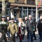 Grupa osób różnej płci i wieku kracząca ulicą w patriotycznym pochodzie. Część osób trzyma biało-czerwone flagi.