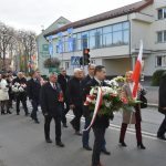 Grupa osób różnej płci i wieku kracząca ulicą w patriotycznym pochodzie. Część osób trzyma biało-czerwone flagi.