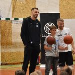 Dwóch młodych mężczyzn ubranych na sportowo stoją na sali gimnastycznej oraz młody chłopak trzyma w rękach dwie piłki do koszykówki kręcące się na długopisach.