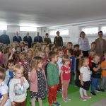 Duża grupa dzieci oraz dorośli, mężczni i kobiety stoją na baczność i śpiewają hymn.