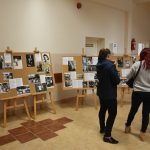 Tablice korkowe stojące na sztalugach na korytarzu. Na nich znajdują się reprodukcje starych fotografii. Obok widac grupę dorosłych kobiet, mężczyznę i kilkuletniego chłopczyka.