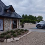 Bus koloru szarego stoi na miejscu parkingowym oznaczonym na niebiesko przed dyżym budynkiem.