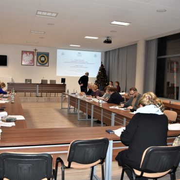 Grupa osób siedzi przy stolikach i słucha mężczyzny który prowadzi preleckję.