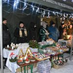Stanowiska na jarmarku z ozdobami świątecznymi na wolnym powietrzu. Widać w nich sprzedawców. Panuje zima.