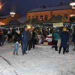 Grupa osób ogląda stoiska na jarmarku na rynku. Panuje zima.